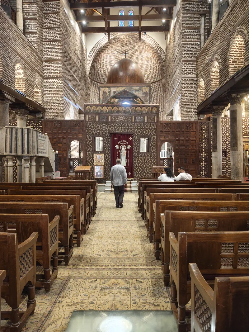 Interior of a Coptic Cairo church with brick arches, carved woodwork, and wooden pews