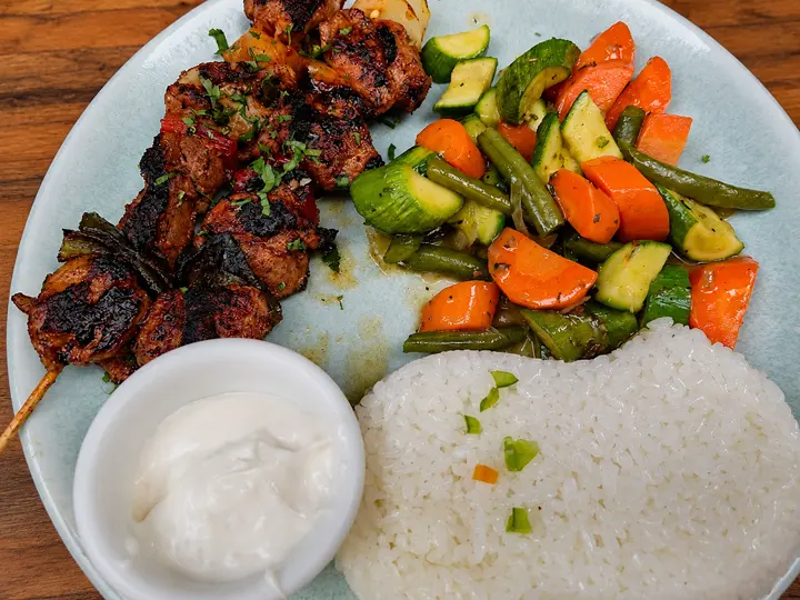 Grilled skewers, rice, vegetables and sauce on a wooden restaurant table